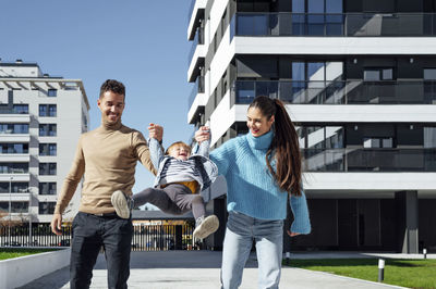 Cheerful parents swinging baby boy in city