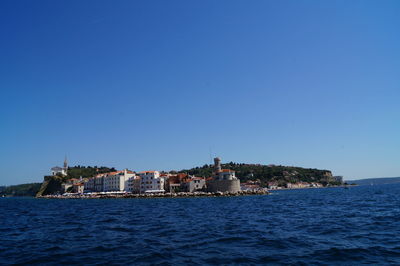 Buildings by sea against clear blue sky