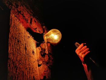 Cropped image of person holding metal by illuminated light bulb mounted on wall
