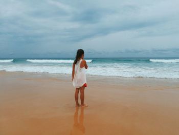 Rear view of woman standing on beach against sky