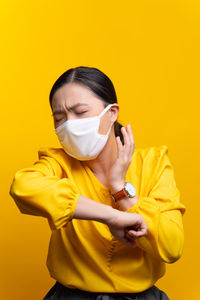 Woman wearing flu mask standing against yellow background