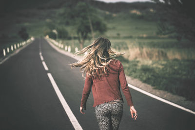 Rear view of woman walking on road during sunny day