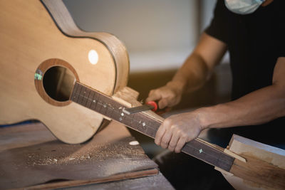 Midsection of man preparing acoustic guitar in workshop