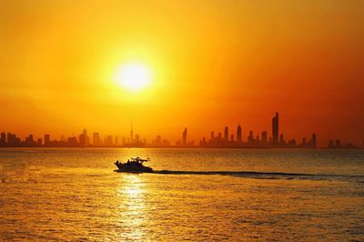 Silhouette boat sailing on sea against orange sky