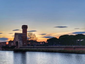 Scenic view of river by buildings against sky during sunset