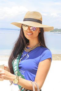 Portrait of young woman wearing hat standing against sky