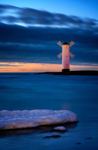 Lighthouse by sea against cloudy sky at dusk