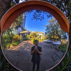 Reflection of man photographing with mobile phone on road mirror