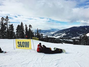 People sitting on mountain against cloudy sky