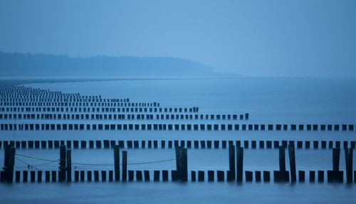 Row of wooden groynes in sea against sky at dusk