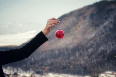 Cropped hand of woman holding bauble against mountains