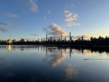 Buildings by river against sky during sunset