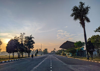 Empty road by trees against sky during sunset