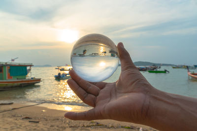 Person holding sunglasses at beach against sky