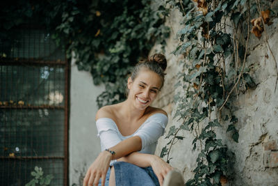 Full length of a smiling young woman sitting against wall