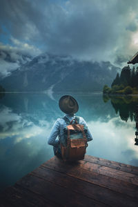 Rear view of man with backpack sitting on pier by lake