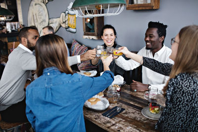 Happy friends toasting drink while sitting at dining table in restaurant