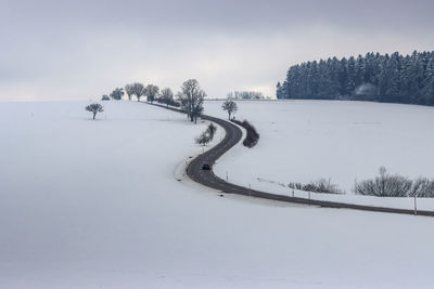 Trees on snow covered field against sky