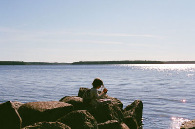 Girl sitting on groyne in sea against sky