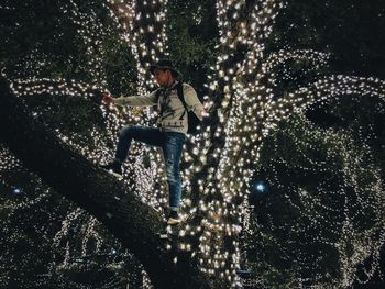 Low angle view of man standing on illuminated tree at night