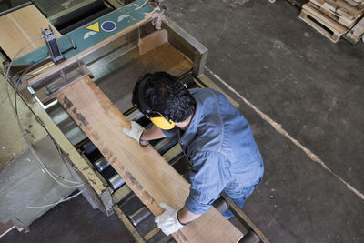 Man with gloves and hearing protectionputting a wood plank on an industrial circular saw in a factory