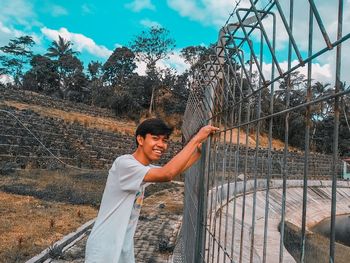 Young woman standing by tree against sky