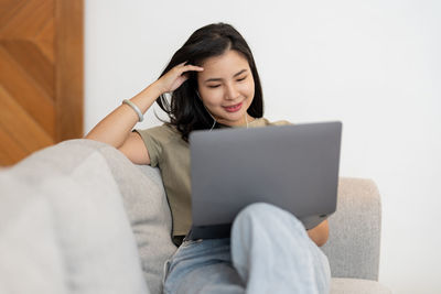 Young woman using laptop while sitting on sofa at home