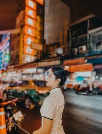 Side view of woman looking away while standing in city