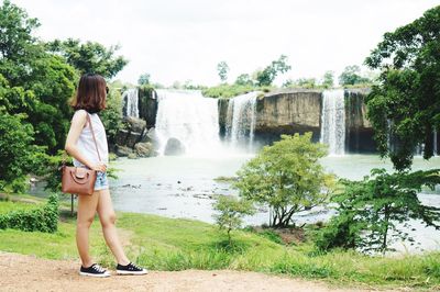 Full length of young woman standing against waterfall