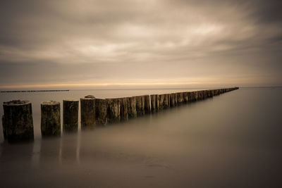 Wooden posts in sea against sky