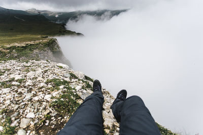 Low section of man on cliff against sky during foggy weather
