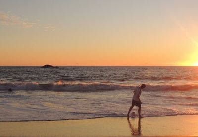 Woman standing on beach against sky during sunset