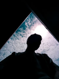 Low angle view of silhouette man against sky seen through window