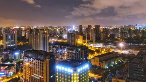 Illuminated modern buildings in city against sky at night