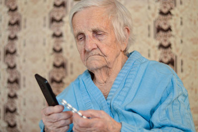 Portrait of a 90-year-old sick pensioner who holds a package of pills and a phone in her hands.