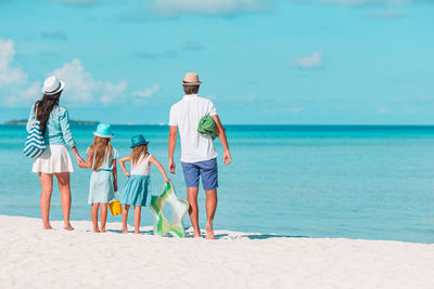 Rear view of people standing at beach against sky