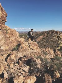 Man sitting on rocky mountain against clear sky