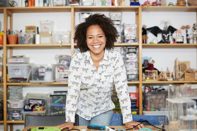 Portrait of confident female technician standing against shelf at workshop