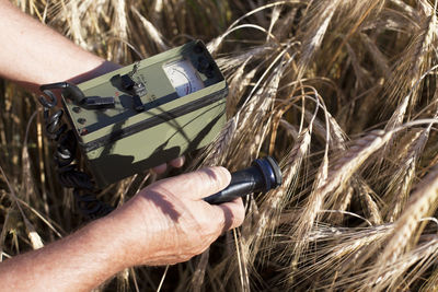 Cropped image of man holding geiger counter on field