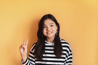 Portrait of young woman standing against yellow background