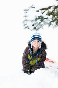 Portrait of cute boy sitting on snow covered land