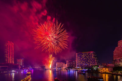 Firework display over illuminated city against sky at night