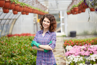 Portrait of young woman with arms crossed standing amidst plants in greenhouse