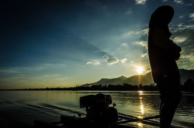 Silhouette person standing by lake against sky during sunset