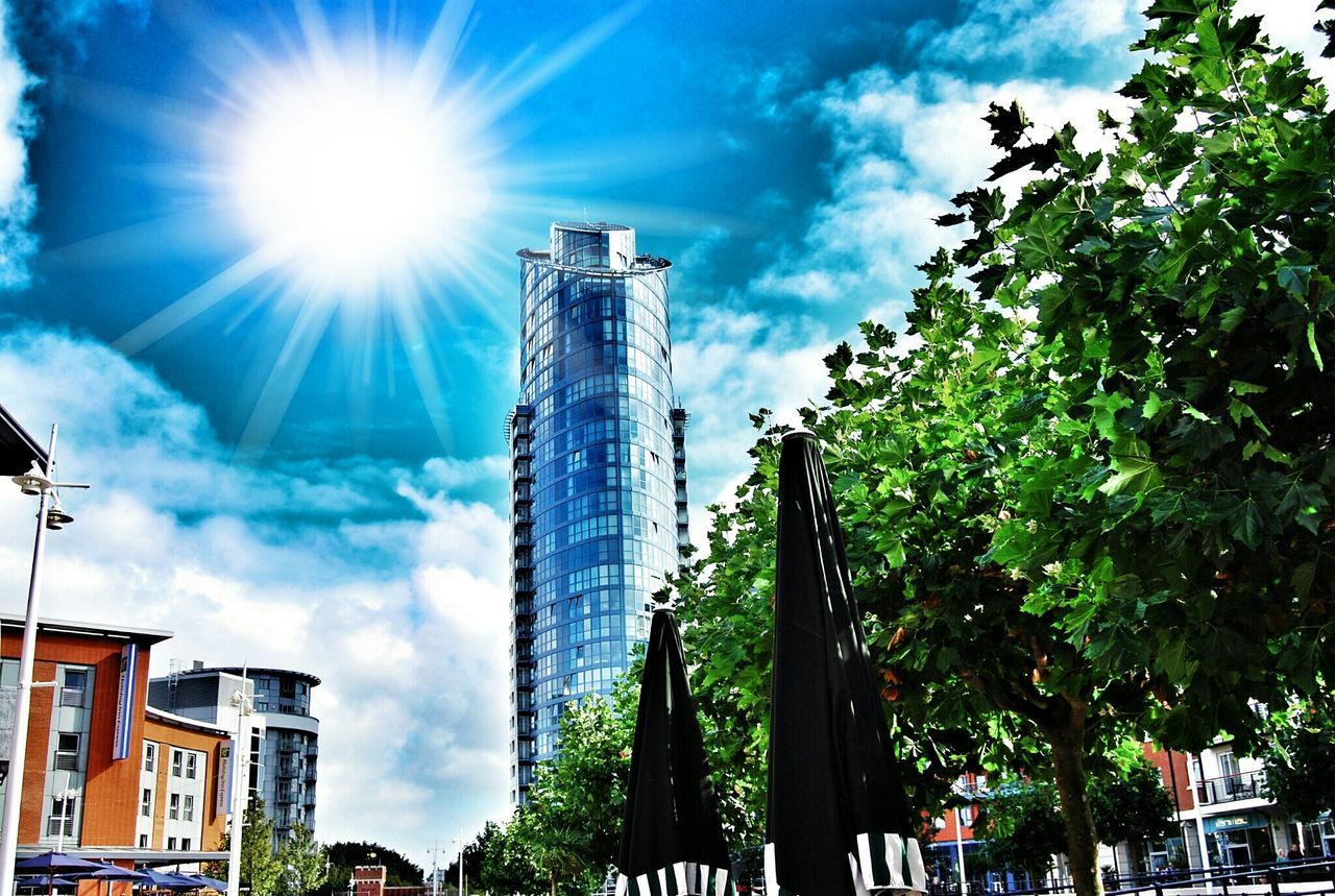 architecture, building exterior, built structure, low angle view, city, tree, sunlight, sky, street light, tall - high, building, blue, sun, day, tower, sunbeam, modern, outdoors, incidental people, skyscraper