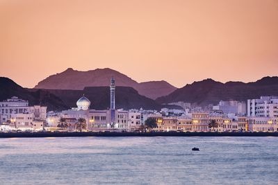 Buildings in city at waterfront during sunset