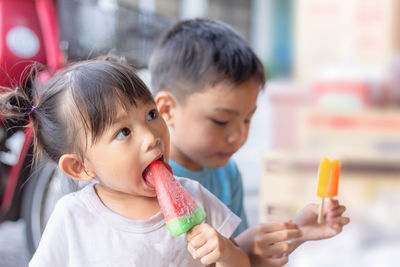 Close-up of siblings eating ice creams while sitting outdoors