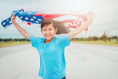Portrait of smiling teenage girl with american flag standing on road