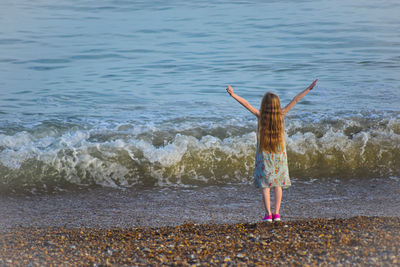 Rear view of girl with arms raised standing on beach