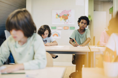 Curious boy drawing with friends at desk in classroom